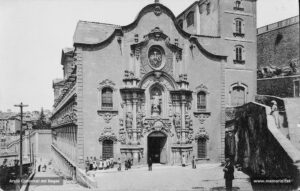 Perspectiva del pòrtic de l'església de la Cova de Sant Ignasi. L'església fou construïda entre els anys 1750 i 1763, però no fou beneïda fins el 1844. L'edifici pertany a l'estil de l'arquitectura anomenada jesuítica. La façana principal que apareix en aquestes imatges és, però, d'inspiració plenament barroca.
Procedència: Arxiu Jaume Pons i Agulló.