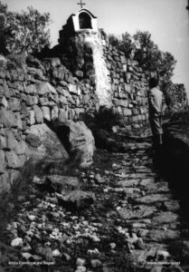 Vista de la desapareguda capelleta existent damunt un marge de pedra seca al camí de la capella de la Guia a la torre de Santa Caterina, els anys vint del segle XX.
Procedència: Arxiu Jaume Pons i Agulló.