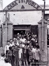 Ramon Junyent, arrambat al pilar dret de l’entrada de la Casa del Poble del Somorrostro, barri de barraques al costat de la Barceloneta (actual Port Olímpic), que formava part del Districte X (Sant Martí). Era una entitat vinculada al Partit Republicà Radical, que es va desvincular de Lerroux i es va adherir a ERC. A la foto també hi apareix Marià Martínez Cuenca (USC). (Família Junyent)